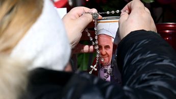 Mujer deja un rosario junto a una vela con un retrato del Papa Francisco / AFP
