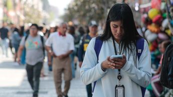 Una mujer camina frente a la catedral de Puebla, con su celular en mano / Agencia Es Imagen